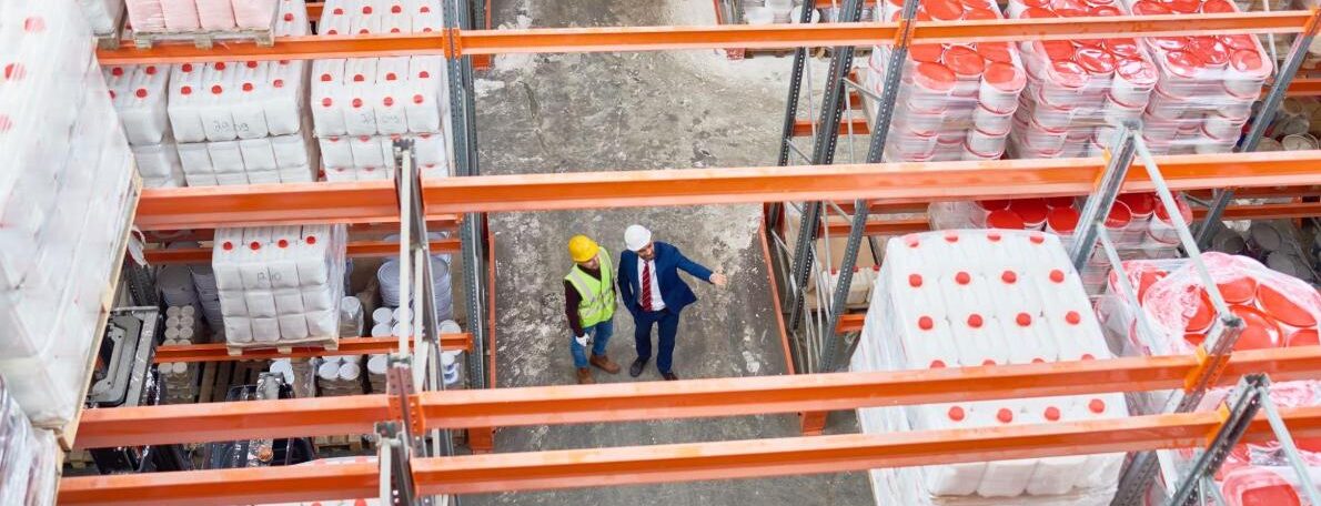 Two Men Stood In Warehouse Pointing at Racking
